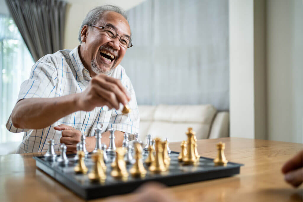 Portrait of Asian Senior Elderly male spend leisure time, stay home after retirement. Happy smiling Old man enjoy activity in house play chess game with friend. Hospital Healthcare and medical concept