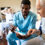 nurse sitting on bed and giving instructions to senior patient when to take his pills in nursing home