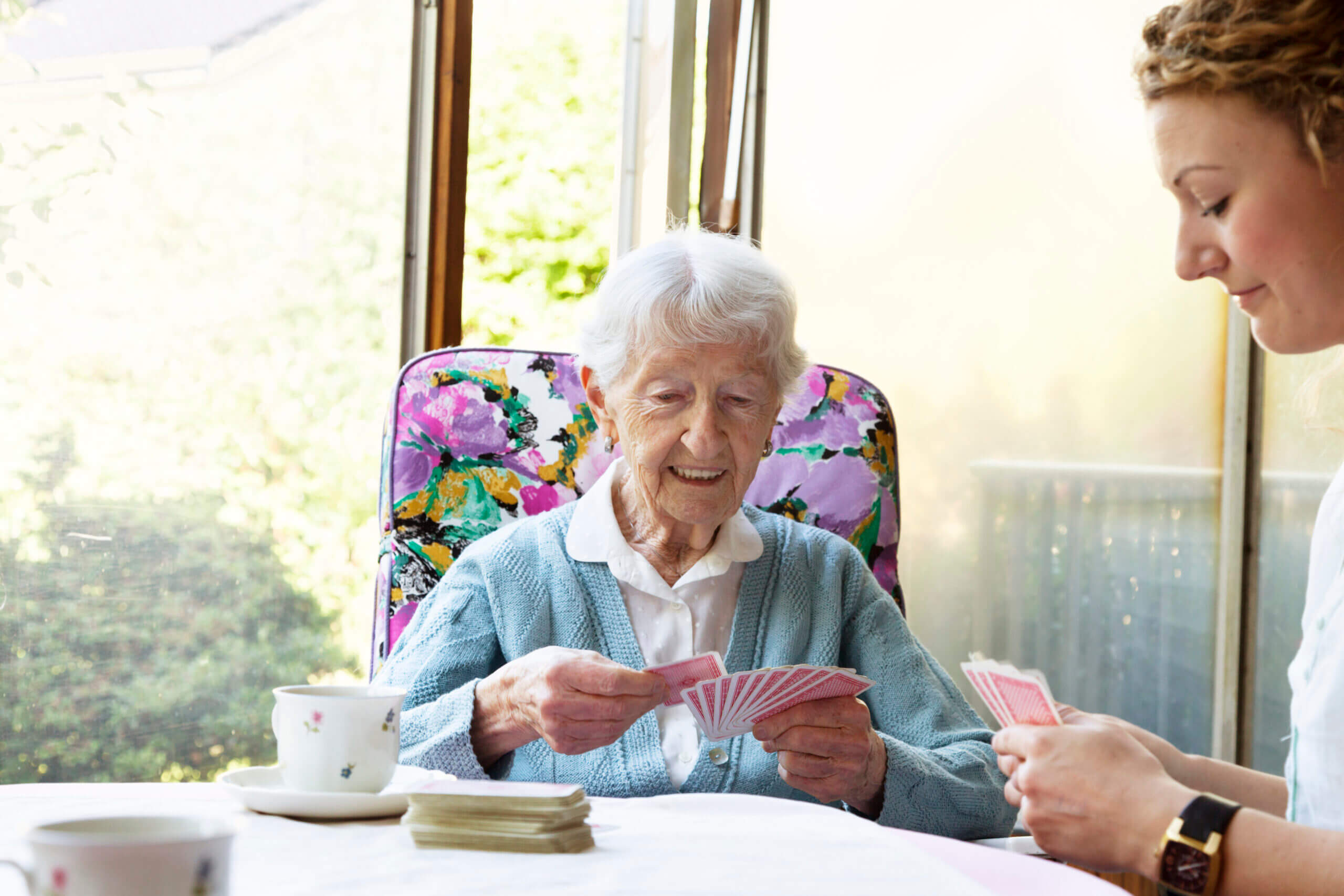 senior woman, 90 years old, and young caregiver playing cards and having fun