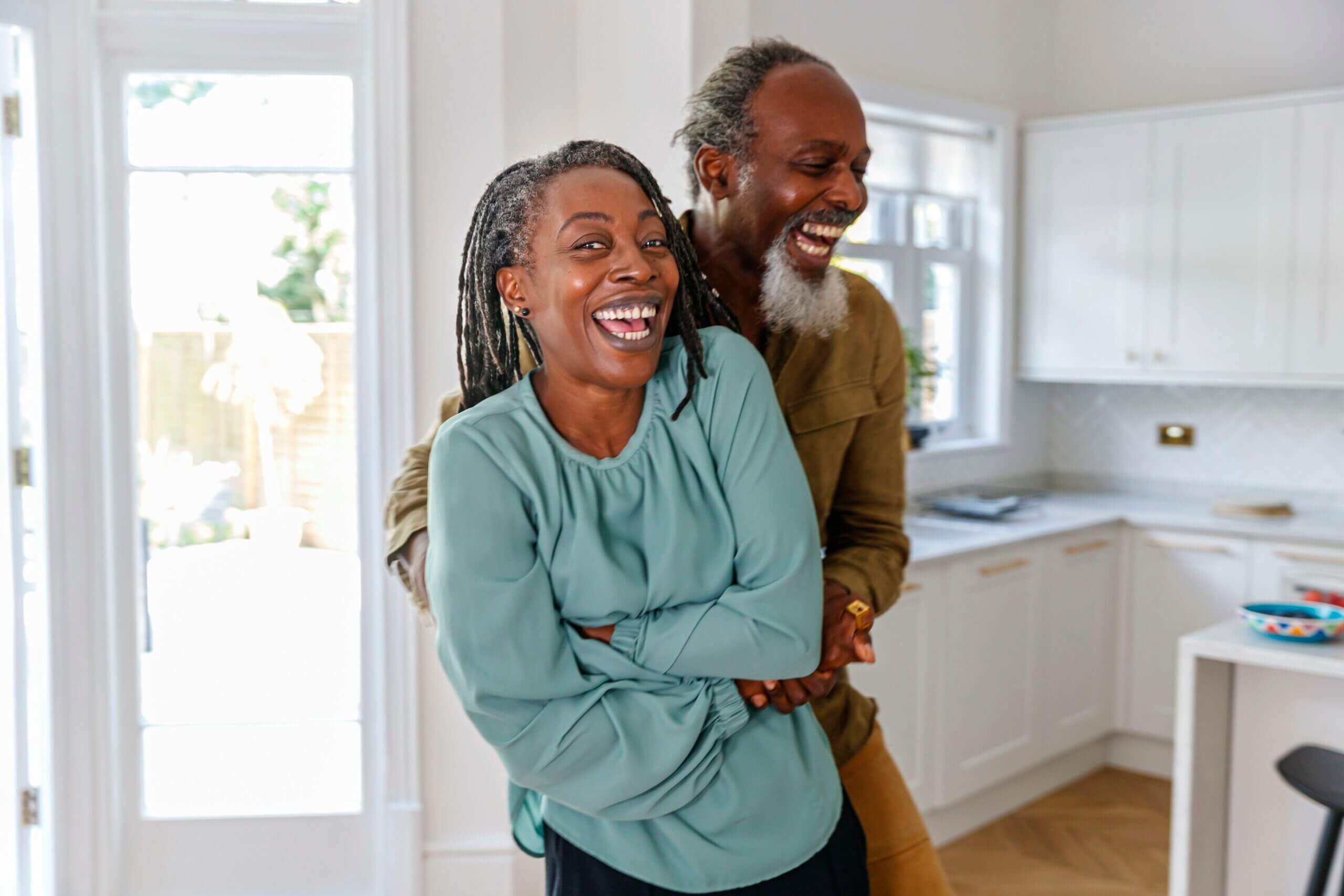 A healthy and happy black senior couple laugh while embracing. The retired active seniors are enjoying a relaxing day at home together. Aging process, retirement, family lifestyle and active seniors concepts