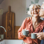 Senior couple for Christmas at home. They are standing in front of kitchen window and drinking tea or coffee.