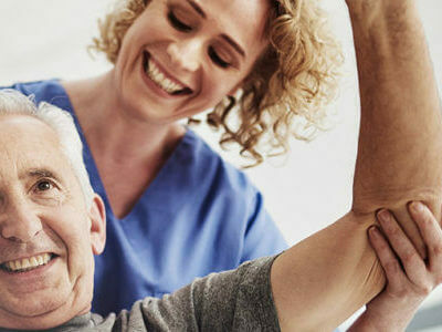 physical therapist/nurse helps an older man with one of his exercises