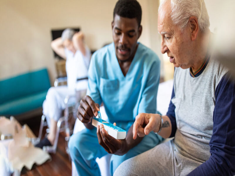 nurse sitting on bed and giving instructions to senior patient when to take his pills in nursing home