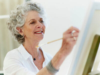 Senior woman smiling while painting on canvas
