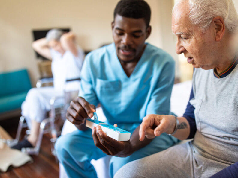 nurse sitting on bed and giving instructions to senior patient when to take his pills in nursing home