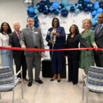 Group of executives line up to cut the ribbon during a grand opening event.
